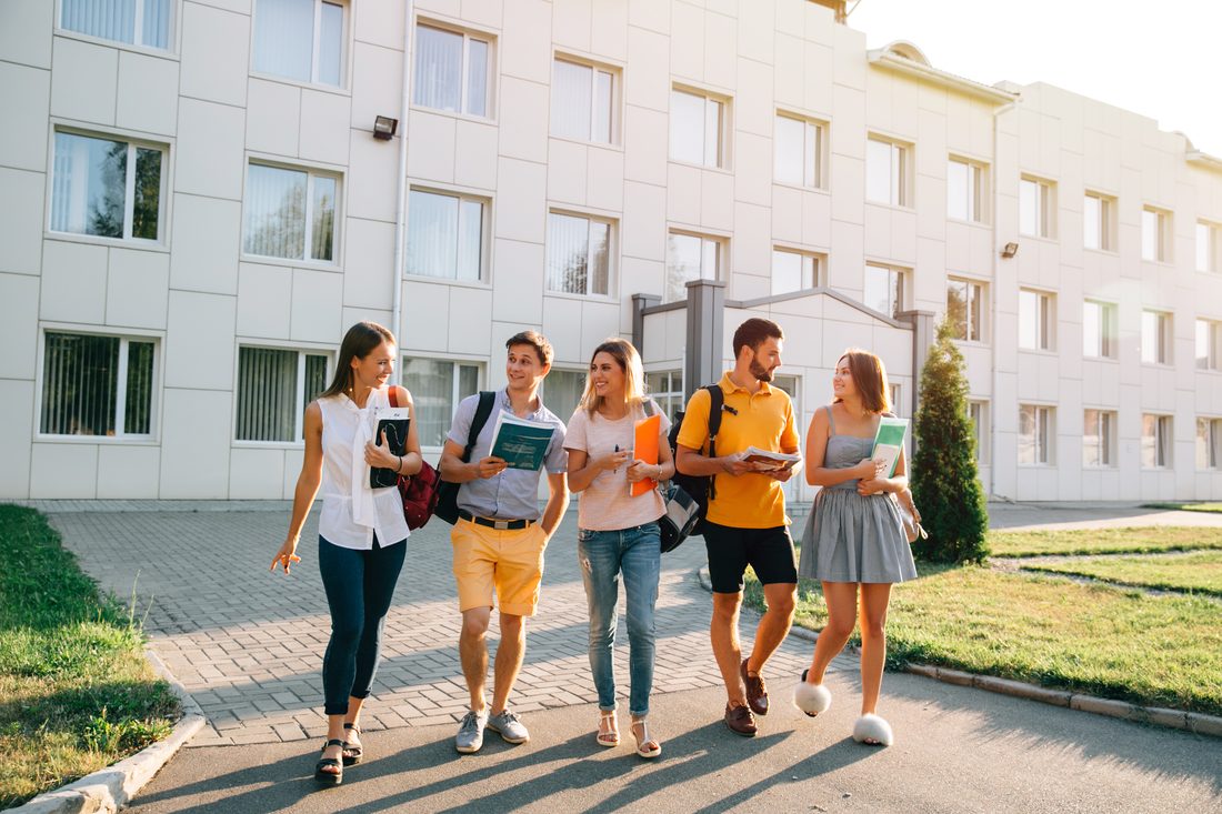 Pięcioro studentów idzie alejką przed budynkiem uczelni